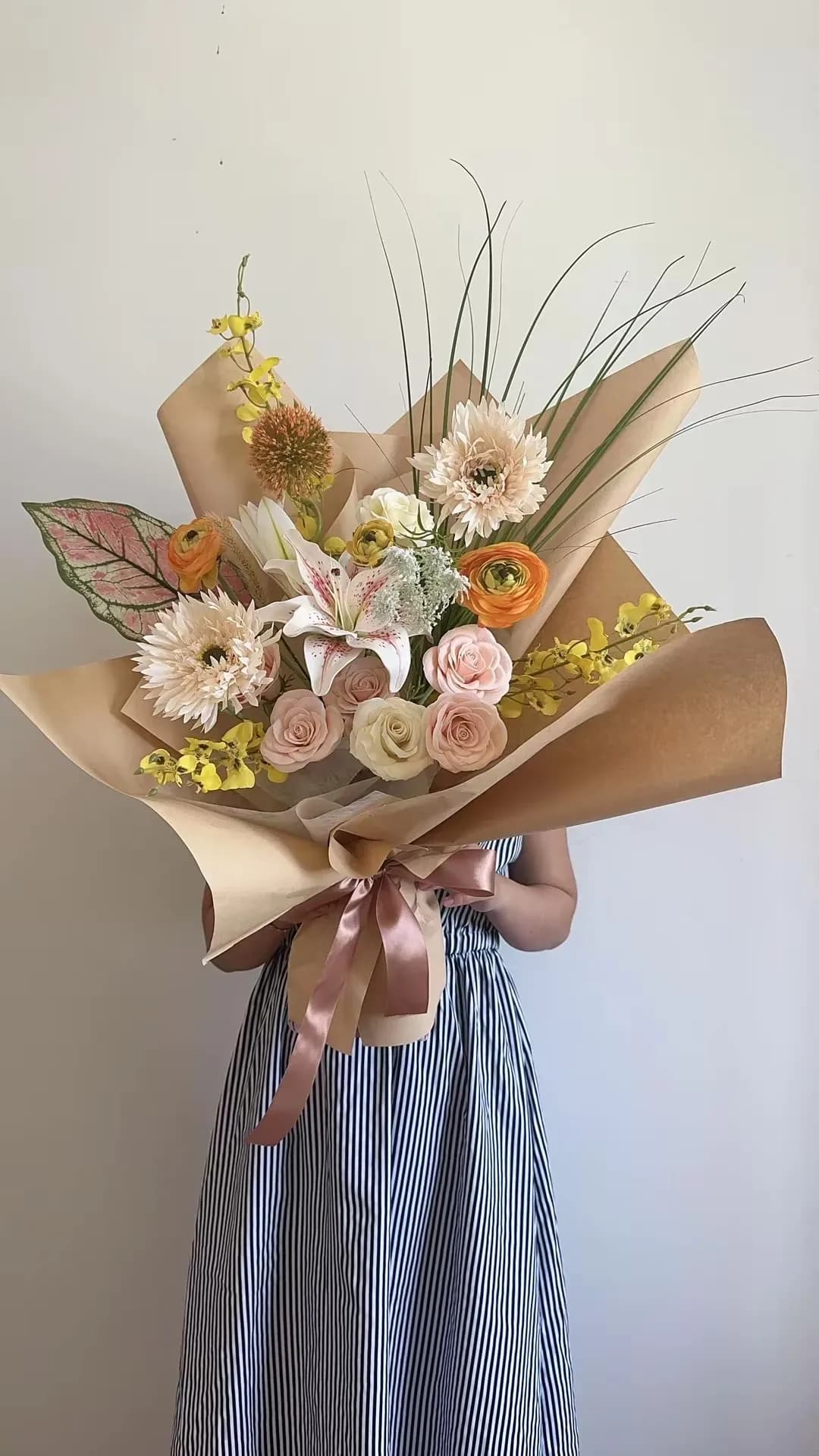 Bó hoa cam vàng phối hồng phấn và trắng kem, điểm ly trắng hồng, lá mảnh vươn cao, giấy kraft và nơ hồng đất.