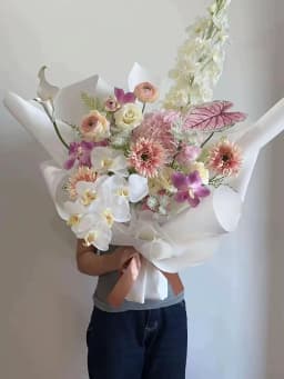 Bó hoa hồng trắng dáng cao, phối cẩm tú cầu hồng và lan tím, dải lan trắng phía trước, giấy trắng và nơ hồng đất.