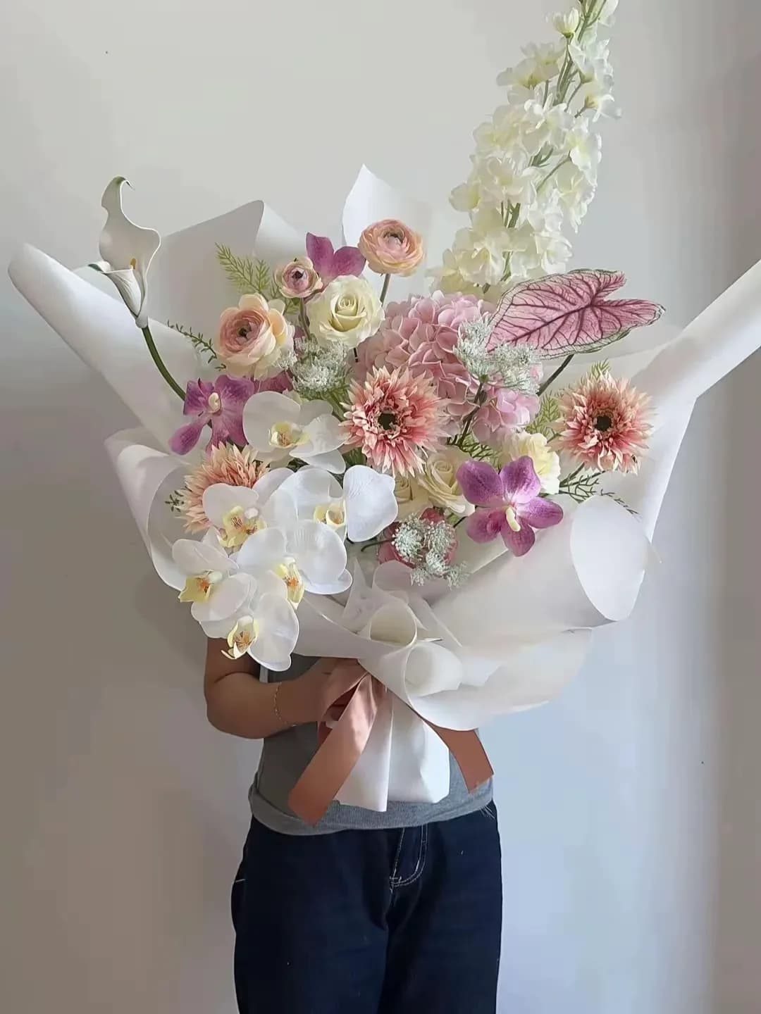Bó hoa hồng trắng dáng cao, phối cẩm tú cầu hồng và lan tím, dải lan trắng phía trước, giấy trắng và nơ hồng đất.